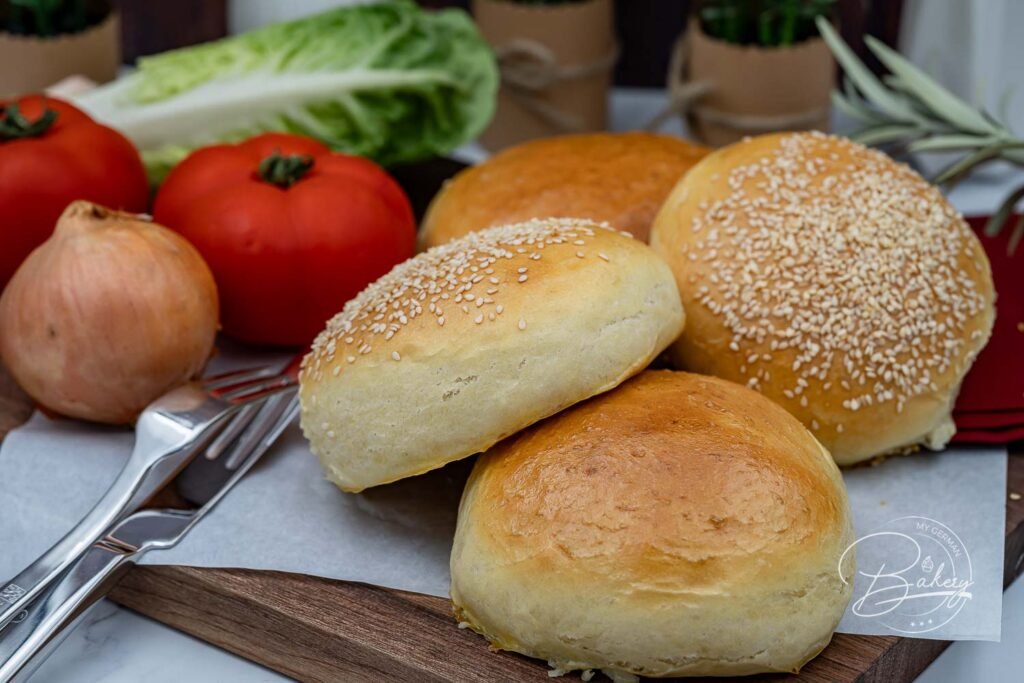 Selbstgemachte Burger Buns – eine Hälfte mit Sesam, die andere ohne, auf Backpapier - Burger Buns mit Sesam und ohne - weiche Brioche Burger Buns Rezept