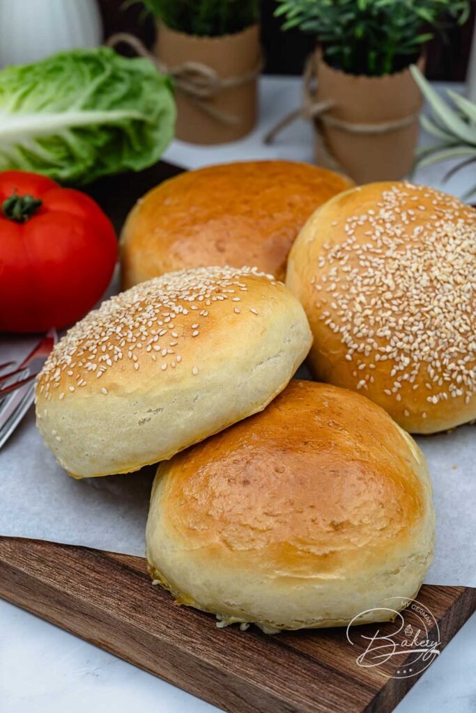 Frisch gebackene weiche Brioche Burger Buns mit Sesam auf einem Holzbrett - weiche Brioche Burger Buns selbstgemacht - Brioche Burger Buns Rezept